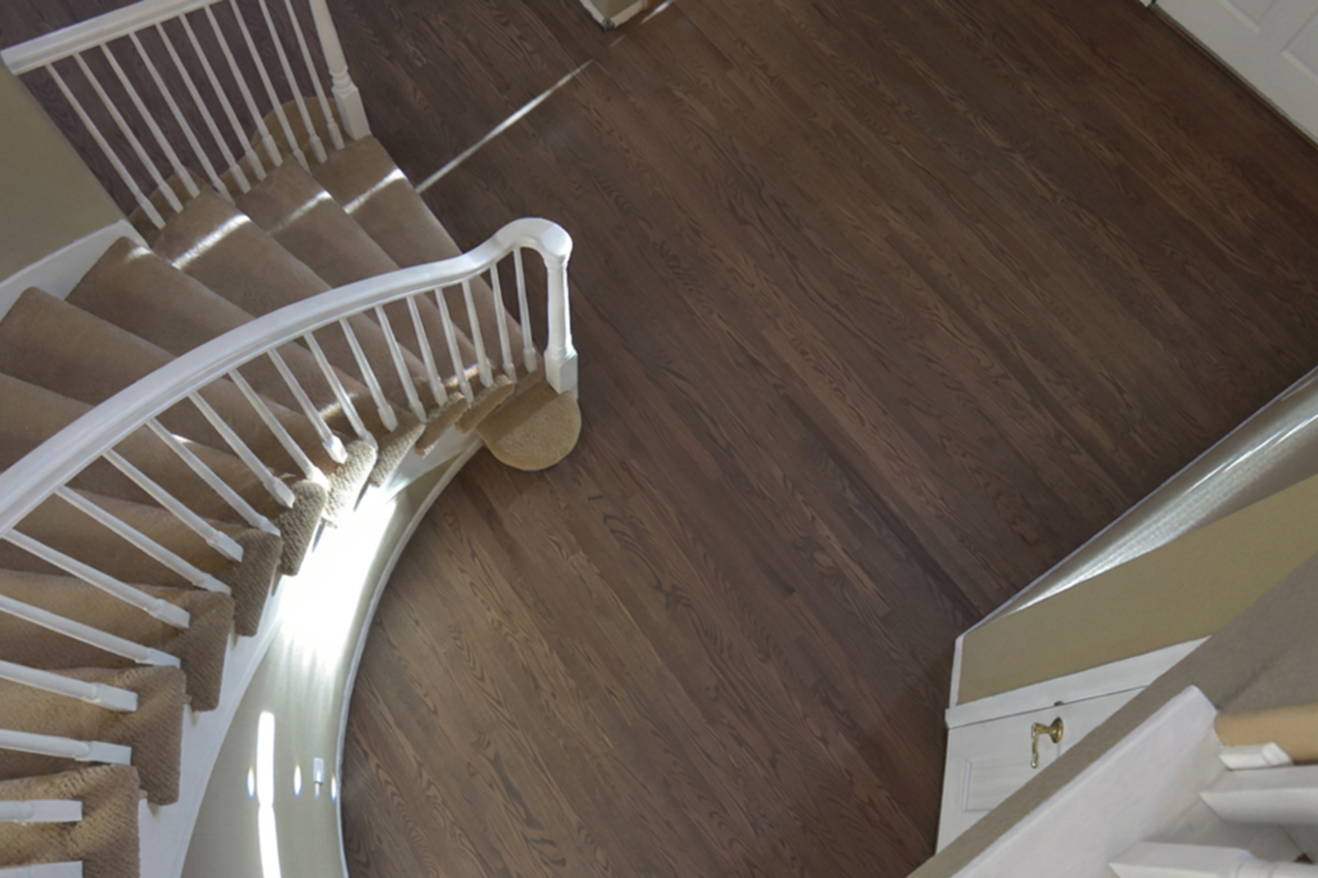Red oak floor colored with a custom gray and brown Bona stain mix beside a curved staircase